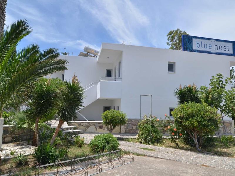 Bílá hotelová budova s palmami a keři pod modrou oblohou.