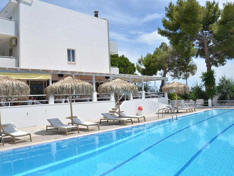 Moderní hotelový bazén s lehátky a slaměnými slunečníky, obklopen stromy a jasnou oblohou.