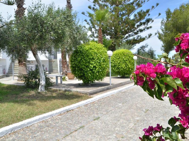 Dlážděná cesta vede zahradou se zelenými stromy a růžovými květy v hotelové oblasti.