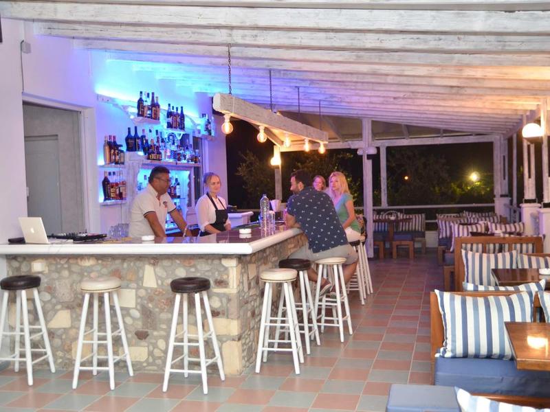 Útulný bar s bílými stoličkami, modrým podsvícením a venkovní sezením.