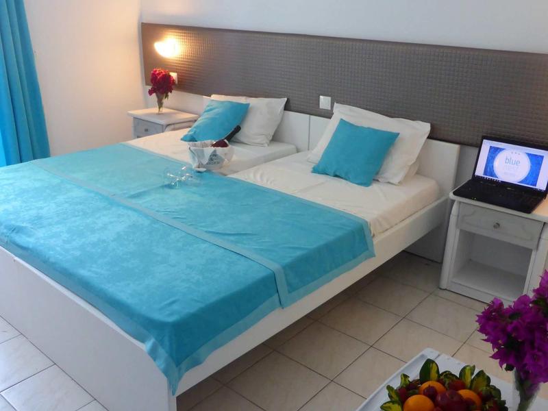 Moderní hotelový pokoj s manželskou postelí, tyrkysovými doplňky a nočními lampami.