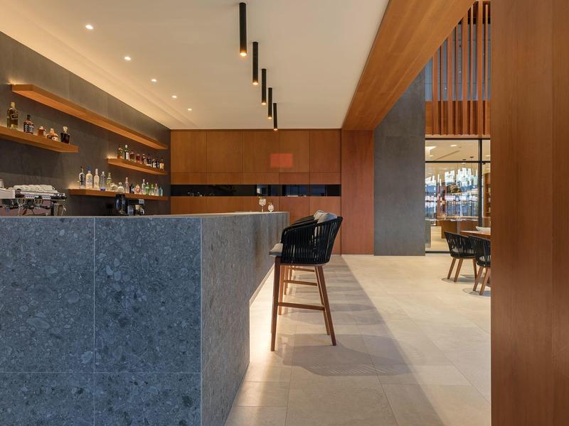 Modern hotel bar area with wooden accents, gray stone counter, and black bar stools.