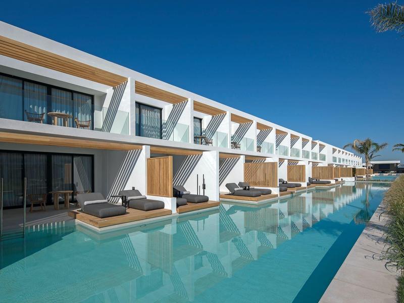 Modern hotel complex with pool and direct access to rooms with loungers.