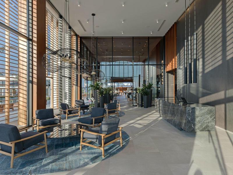 Bright, modern hotel lounge area with seating and large windows with blinds.