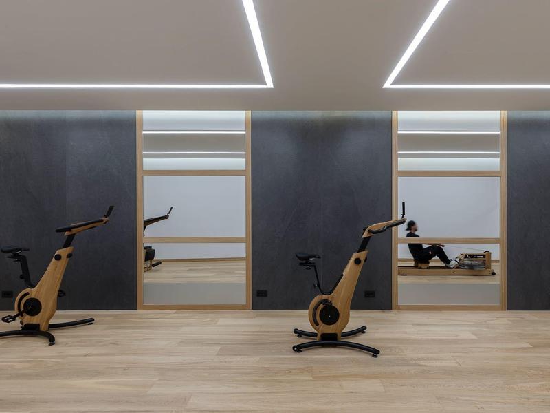 Modern gym room with exercise bikes, wooden floor, and large wall mirrors.
