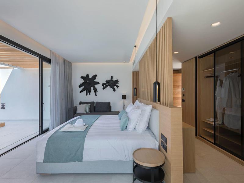 Modern hotel room with large bed, glass wall, and contemporary furnishings.