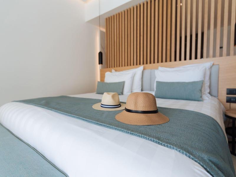 Modern hotel room with large bed, wooden wall, and two hats on the blanket.
