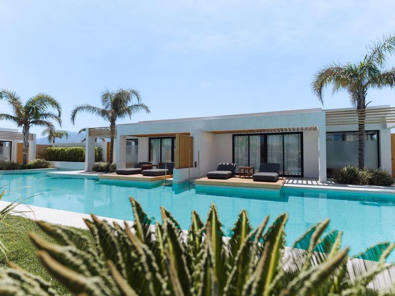 Modern bungalow with large pool and palm trees under a blue sky.