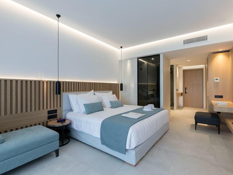 Modern hotel room with double bed, bench, lighting, and desk.