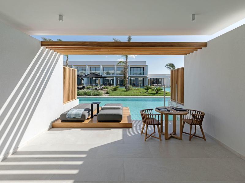 Modern courtyard with lounge furniture and dining table next to a pool in a hotel setting.