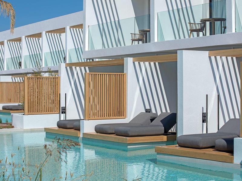 Modern hotel rooms with private terraces and loungers directly by the pool under a blue sky.