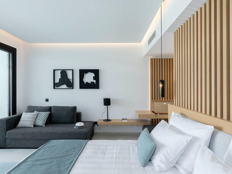 Modern hotel room with bed, sofa, wooden wall, and minimalist decor.