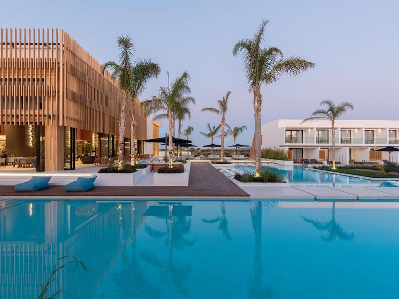 Modern hotel pool with lounge chairs and palm trees under clear sky at sunset.
