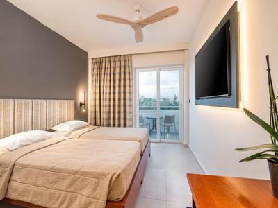 Stilvolles Schlafzimmer mit Doppelbett, grauer Wand, Ventilator und Balkon mit Stadtblick.