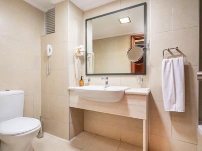 Hell gefliestes Badezimmer mit Toilette, Waschbecken, großem Spiegel und Handtüchern.