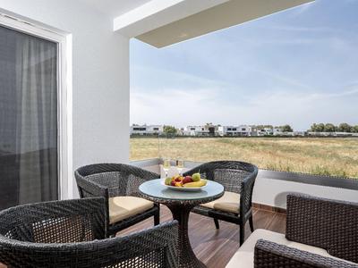 Balkon mit Rattanstühlen und kleinem Tisch mit Getränken, Blick auf Feld und Häuser im Hintergrund.