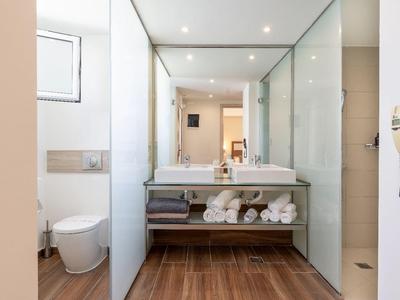 Modernes Badezimmer mit Holzfußboden, großem Spiegel und weißem Waschbecken mit Handtüchern.