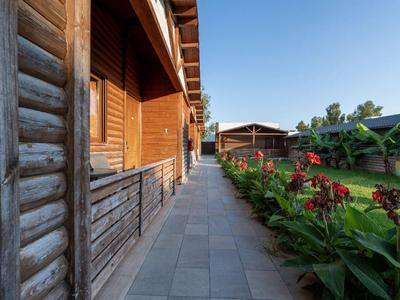 Ein Weg entlang einer Holzhütte mit Blumenbeeten und weiteren Gebäuden im Hintergrund bei klarem Himmel.