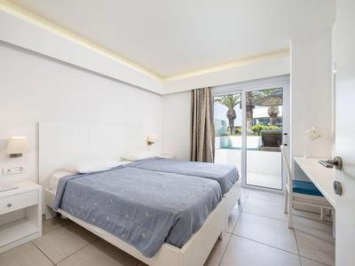 Helles Hotelzimmer mit Doppelbett, weißen Möbeln und Blick auf Terrasse und Garten.