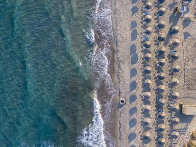 Blick von oben auf einen Strand mit geordneten Sonnenschirmen und Liegen neben dem Wasser