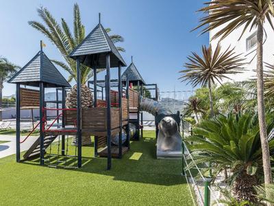 Moderner Spielplatz mit Holztürmen, Rutschen und Klettergerüst unter klarem Himmel.
