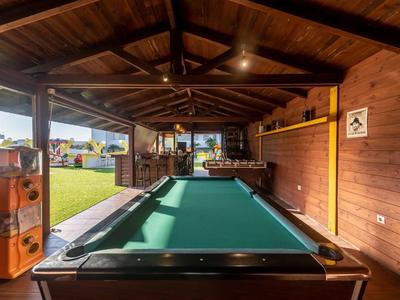 Innenbereich mit Billardtisch und Holzverkleidung, angrenzend an einen Garten mit Blick auf das Meer.