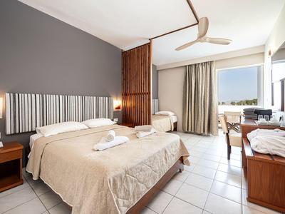Helles Hotelzimmer mit Doppelbett, Einzelbett, Ventilator und Blick auf den Balkon.