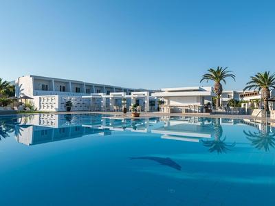 Moderner Hotelpool mit klarem Wasser, weißem Gebäude und Palmen bei blauem Himmel.