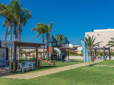 Hotelgarten mit Spielplatz, Palmen und blühendem Rasen unter klarem blauem Himmel.