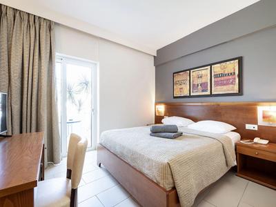 Modernes Hotelzimmer mit Doppelbett, Schreibtisch, Stuhl und Zugang zu einem Balkon mit Vorhängen.