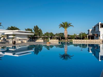 Großer Hotelpool mit klarem Wasser, umgeben von weißen Gebäuden und Palmen unter klarem Himmel.