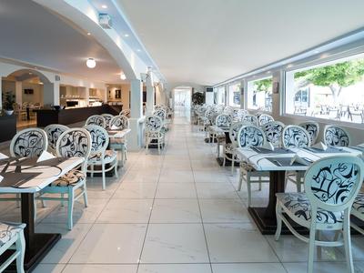 Heller, moderner Speisesaal mit weißen Stühlen und großen Fenstern in einem Hotel.