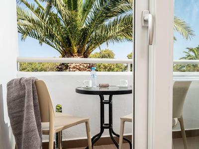 Balkon mit Tisch, zwei Stühlen und Blick auf Palmen bei klarem Himmel.