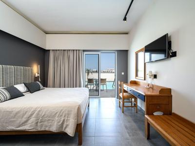 Elegantes Hotelzimmer mit Doppelbett, Schreibtisch, Fernseher und Balkon mit Blick nach draußen.