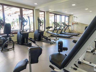 Heller Fitnessraum mit großen Fenstern, mehreren Laufbändern, Ergometern und Kraftgeräten.