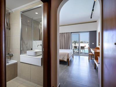 Blick durch Flur in ein Hotelzimmer mit Bett, Balkon und Badezimmer mit Wanne und Waschbecken.