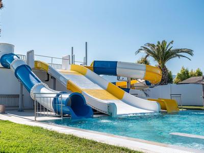 Mehrere bunte Wasserrutschen führen in einen Pool neben einer Hotelanlage mit Palmen.