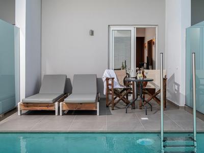 Zwei graue Liegestühle und ein hölzerner Tisch mit Stühlen auf einer Terrasse neben einem Pool.