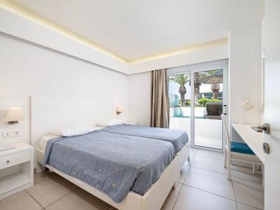 Hell eingerichtetes Hotelzimmer mit Doppelbett, Nachttischen und Blick auf Terrasse.