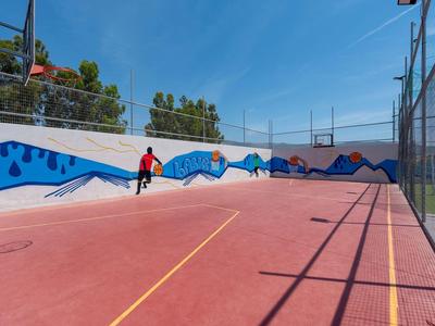 Roter Tennisplatz mit Kettenglazenbegrenzung, bemalter Wand und Person in rotem Hemd.