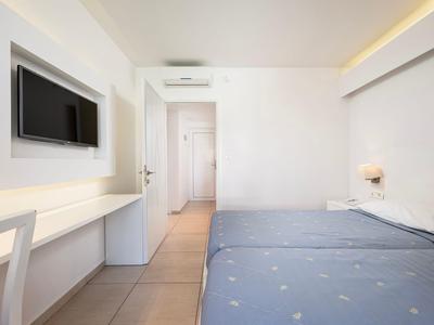 Helles Hotelzimmer mit zwei Einzelbetten, Schreibtisch und Flachbildfernseher an der Wand.