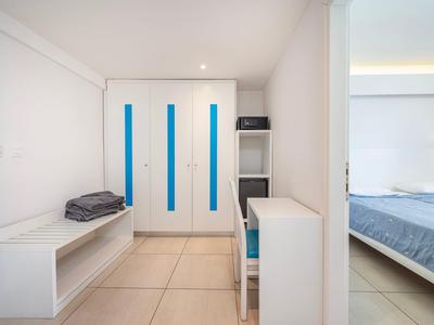 Helles Hotelzimmer mit weißem Mobiliar, großem Kleiderschrank und Blick auf ein Bett.
