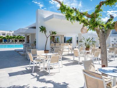 Moderner Hotelaußenbereich mit weißen Stühlen und Tischen neben einem Pool unter blauem Himmel.