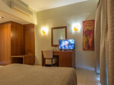 Modern eingerichtetes Hotelzimmer mit Bett, Schreibtisch, Fernseher und Vorhängen am Fenster.