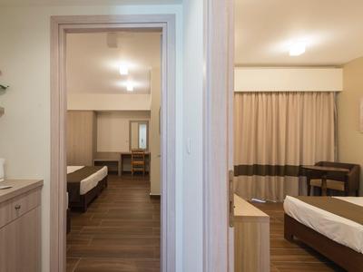 Blick durch zwei Hotelzimmer mit Einzelbetten, hölzernen Möbeln und warmem Licht.