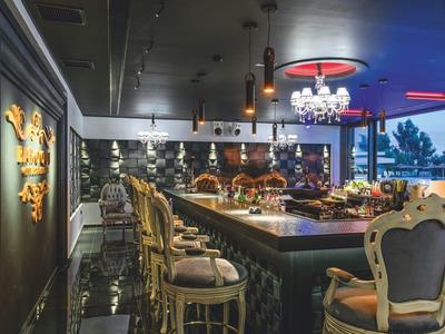 Elegante Bar mit Sitzplätzen, Kronleuchter, Spiegelwand und stilvollem, dunklem Interieur.