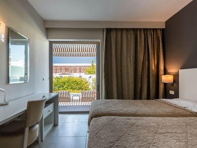 Modernes Hotelzimmer mit Doppelbett, Schreibtisch, Stuhl und Blick auf Balkon mit Pflanzen.