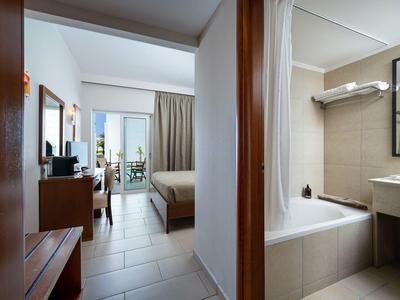 Moderner Hotelgang mit Blick ins Schlafzimmer links und helles Bad mit Wanne rechts, klare Linien, beige Töne.