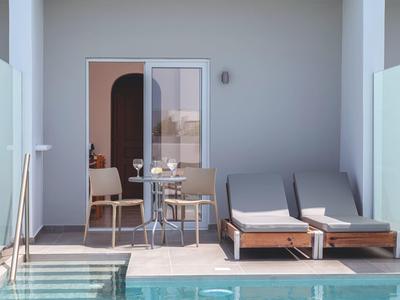 Moderner Außenbereich mit Pool, zwei Sonnenliegen, kleinem Tisch und Stuhl vor einer Glastür.