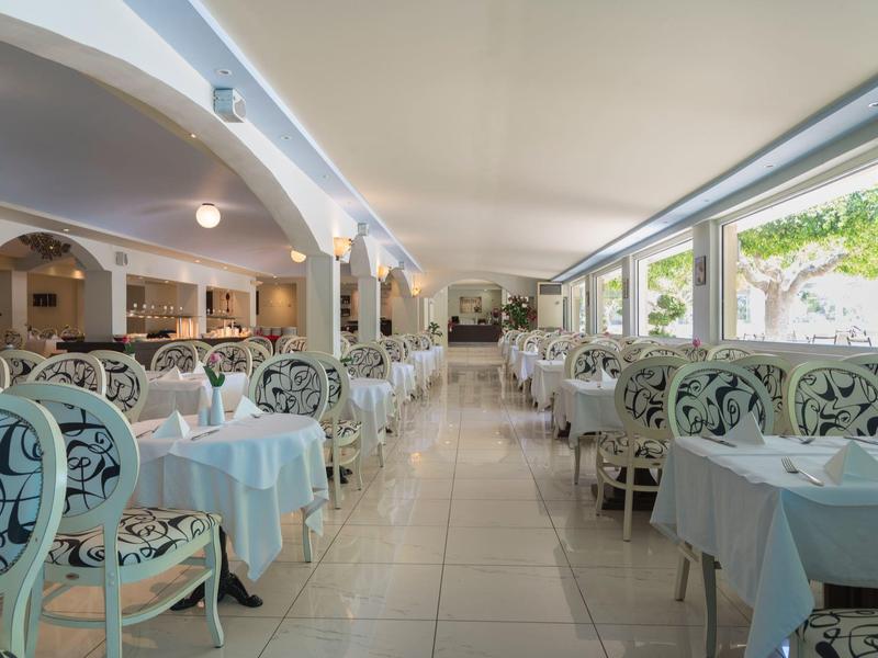 Comedor luminoso de hotel con sillas decorativas y manteles blancos junto a grandes ventanas.